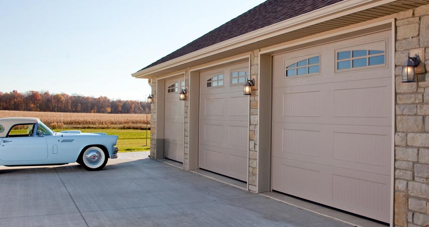 Picture of a stone house with tan garage doors. There is a old blue car on the left.