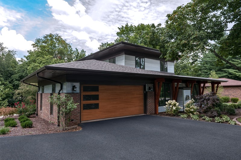 Picture of a brick and metal siding house with a brown garage door with three windows.