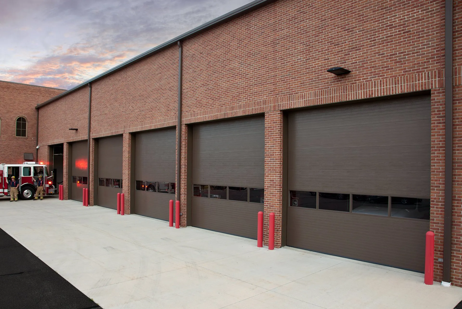 Picture of a red brick fire station with black garage doors.