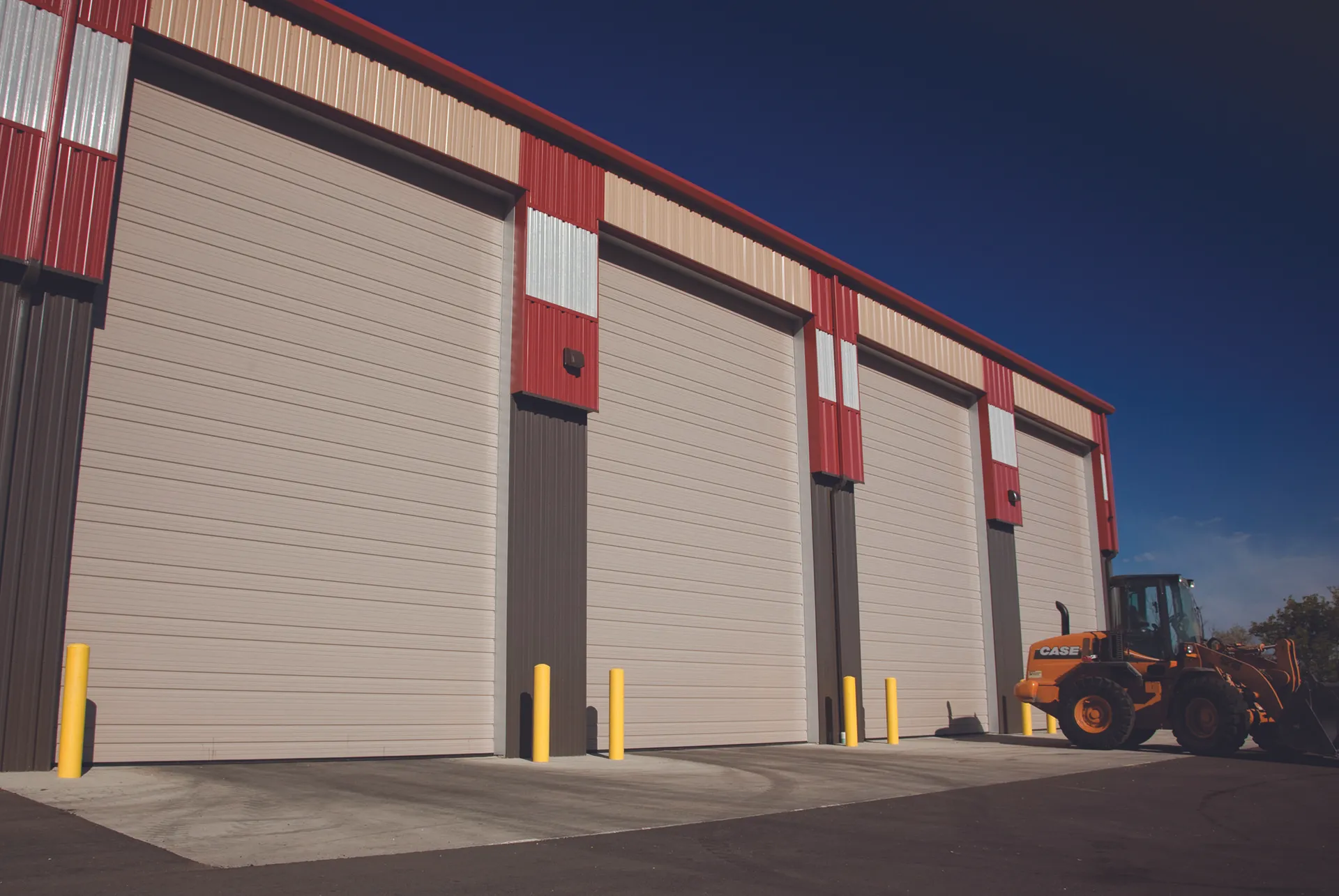 Picture of a red, beige, and gray warehouse with four large grey garage doors.